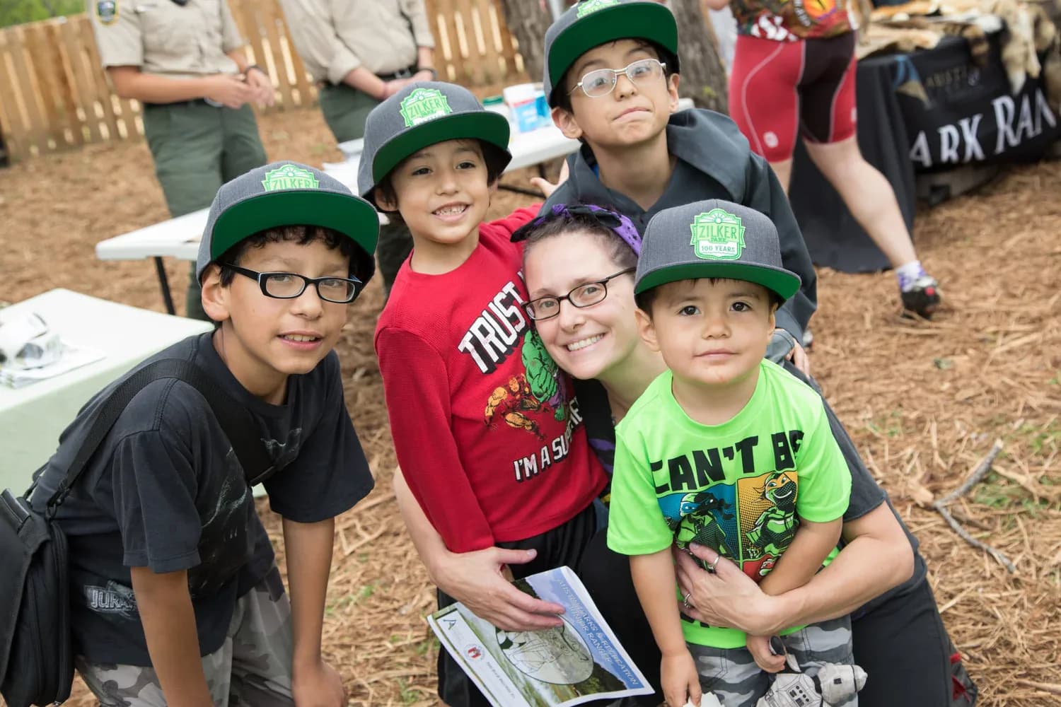 Children in junior park ranger caps posing with a volunteer at a park event