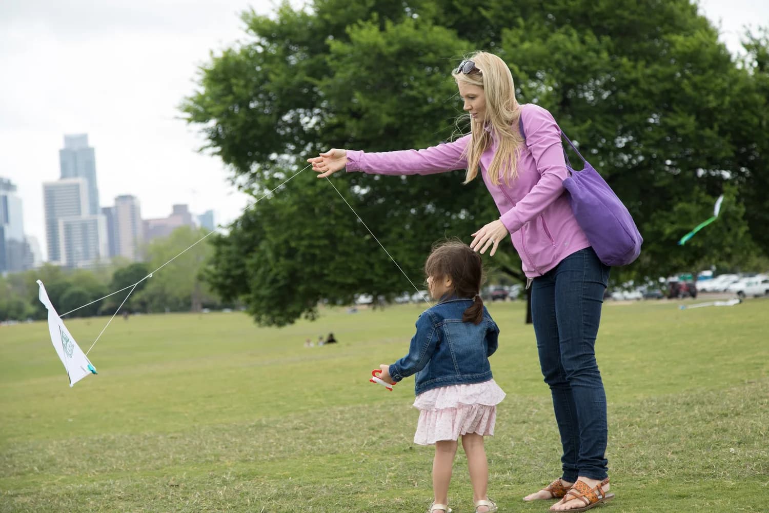 A parent and child flying a kite on the Great Lawn with the Austin skyline behind