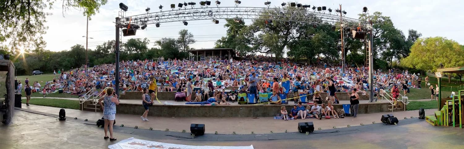 A packed audience filling the Zilker Hillside Theater at dusk for a performance