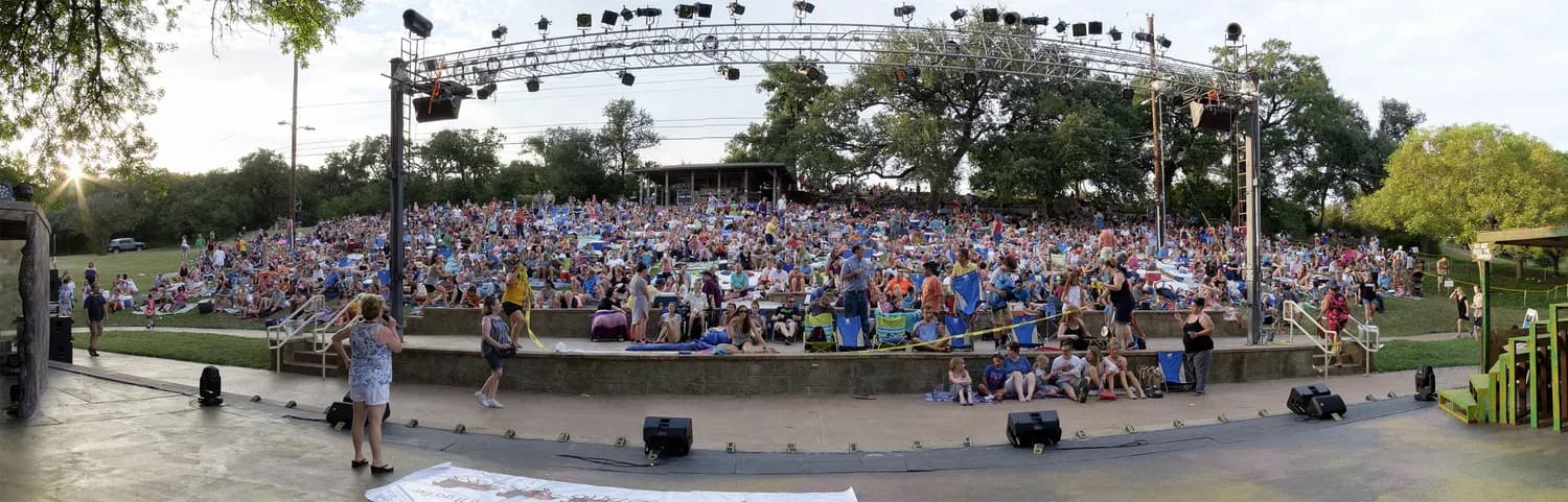 A packed audience filling the Zilker Hillside Theater at dusk for a performance
