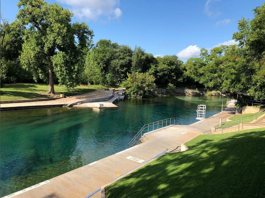 The calm upstream end of Barton Springs Pool lined with trees and limestone