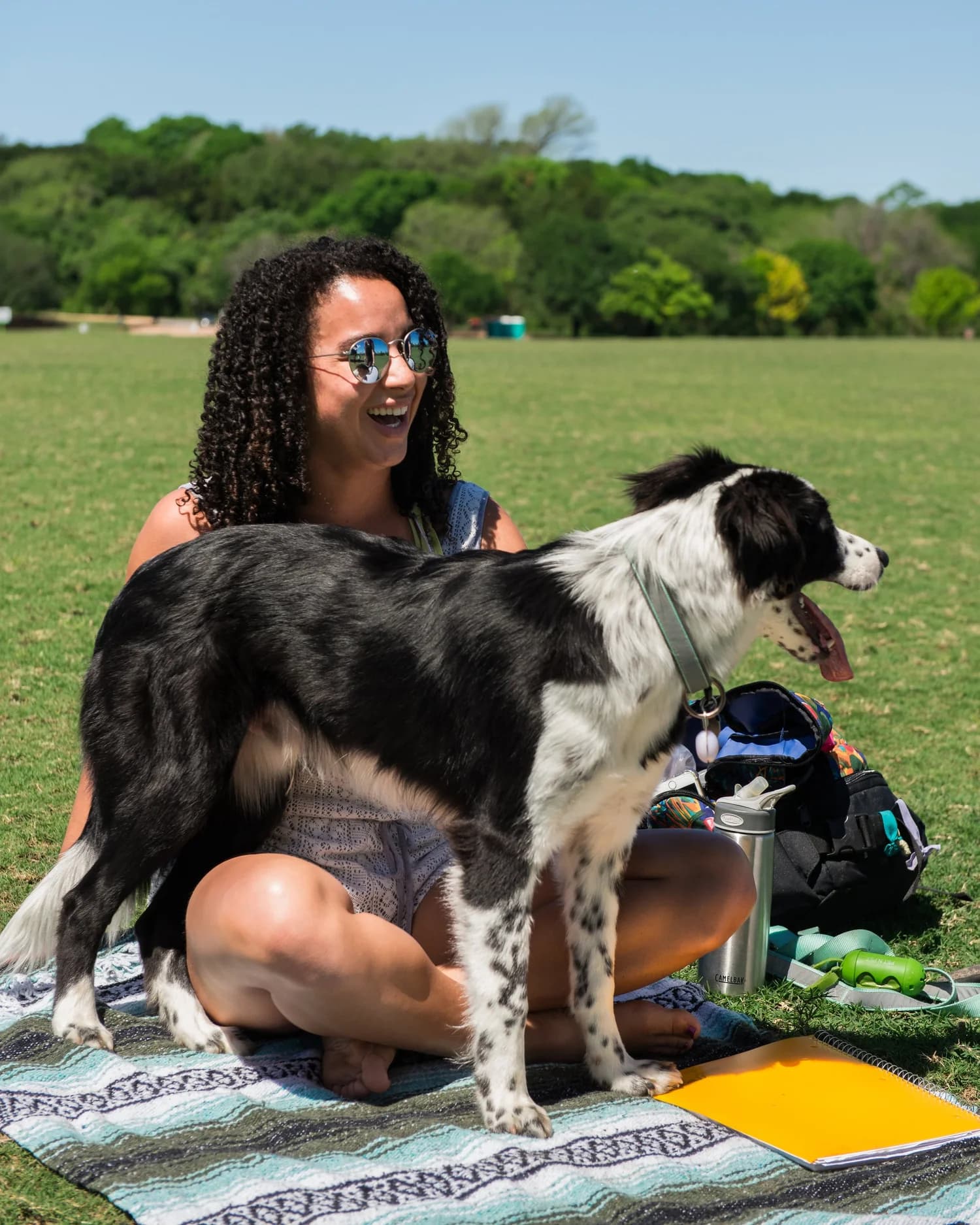 A woman laughing on a picnic blanket on the great lawn with her dog