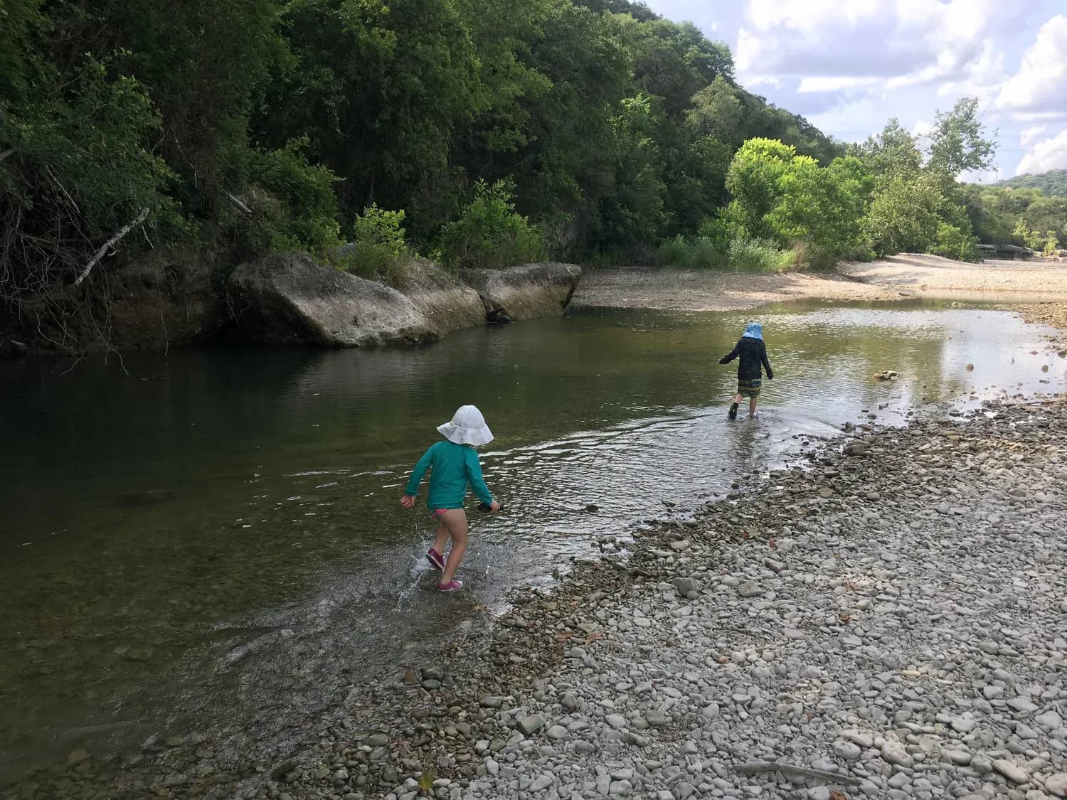 Two children in sun hats wading across the shallows of Barton Creek