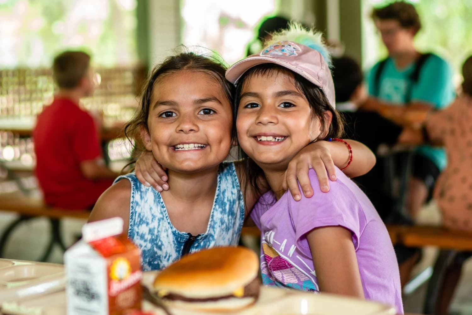 Two young girls smiling together at a summer day camp in the park