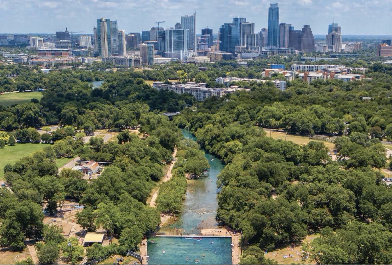 Aerial view of Barton Springs and Zilker Park with the downtown Austin skyline beyond