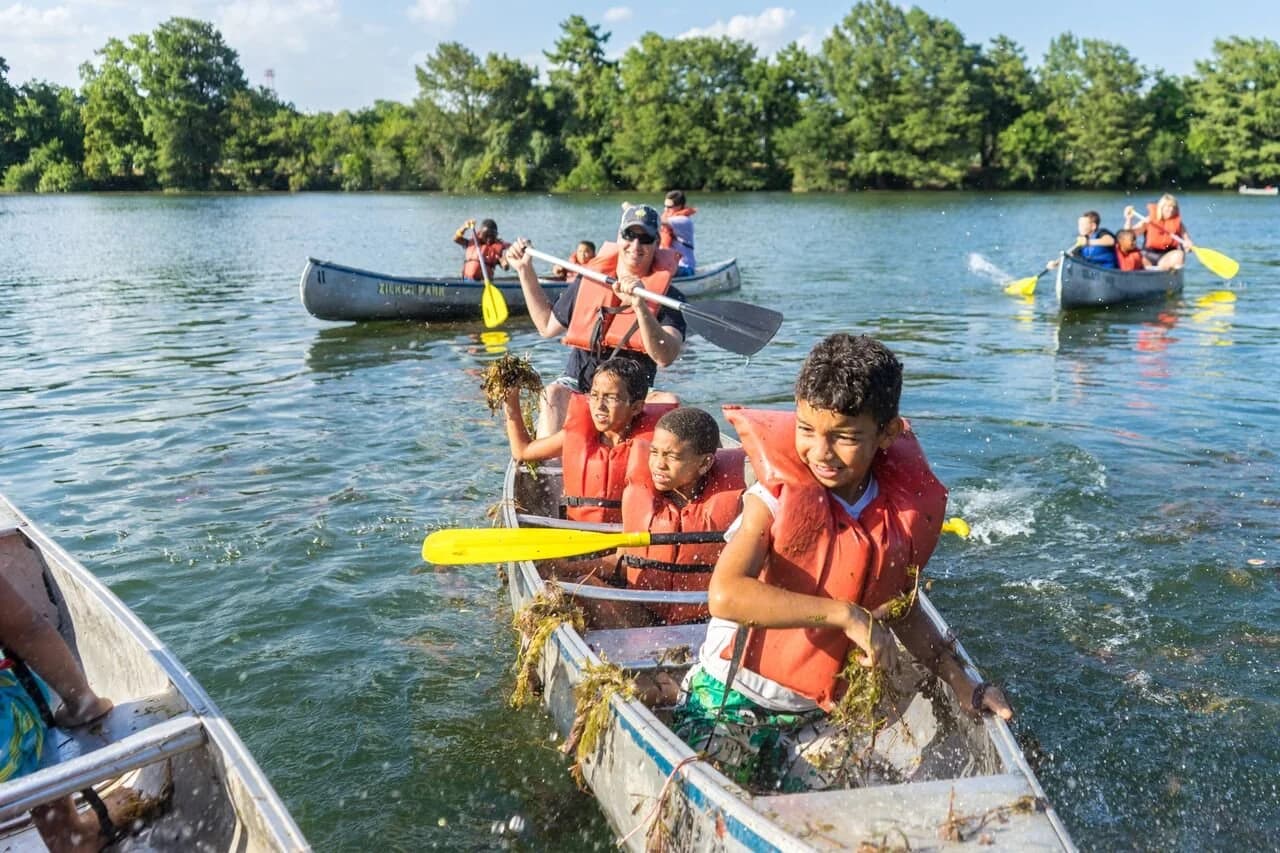 Children in life jackets paddling canoes on the lake at Austin Sunshine Camps