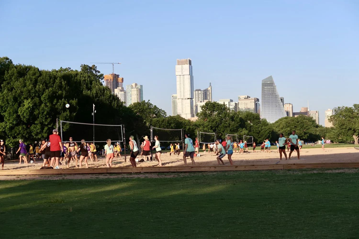People playing volleyball on the sand courts at Zilker Park with the downtown Austin skyline behind